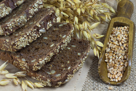 Black bread with sesame seeds and sunflower seeds, oats spikelets and grains of wheat in a wooden spoonの写真素材