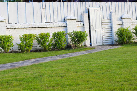 Wooden door and fence of brick and wood, painted in white. green grass and bushesの写真素材