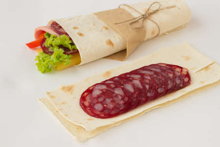 Roll tortilla with herbs, cheese and meat on a white backgroundの写真素材