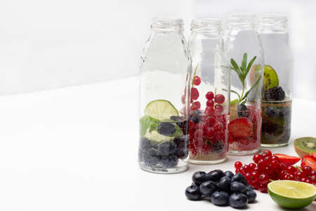 Sparkling red currants, strawberries, blueberries and blackberries water in glass bottles. Berries on table. copyspace. white backgroundの写真素材