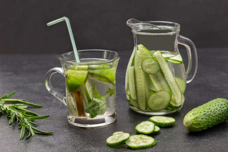 Kiwi and lime infused water in glass. Cucumber infused water in glass jug. Sprig of rosemary and cucumber on table. Black background.の写真素材