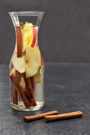 Cinnamon and apple infused water in a glass bottle. Cinnamon sticks on table. copyspace. Black background.の写真素材