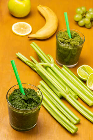 Green smoothie and straw in glasses. Celery stalks and banana on table. Bright mustard background. top viewの写真素材