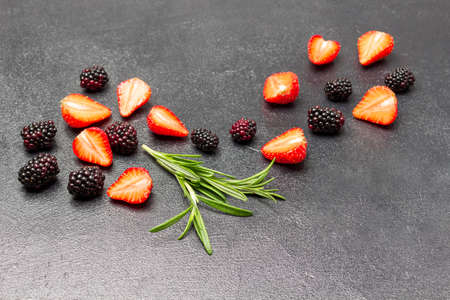 Blackberries and strawberries, sprig of basil on black background. copyspace. top viewの写真素材