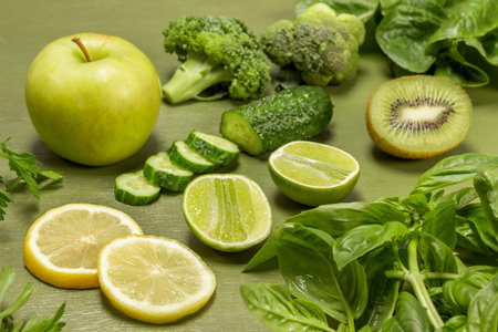 Chopped cucumber, kiwi and lime halves, an apple. Broccoli, basil sprigs and lettuce on the table. close up. top view. green backgroundの写真素材