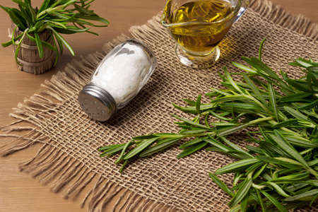 Green rosemary, salt and olive oil in glass bowl on burlap napkin. top view. brown backgroundの写真素材