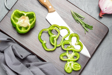 Kitchen knife and chopped green pepper on cutting board. Half an onion and gray napkin. flat lay....