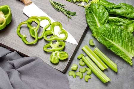 Lettuce leaves and celery stalks on the table. Kitchen knife and chopped green pepper on cutting board. flat lay. gray background.の写真素材