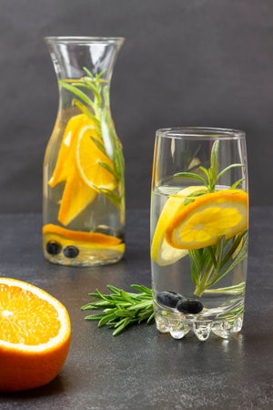 Half orange and sprig of rosemary on table. Orange infused water in glass and bottle. top view. Black background.の写真素材