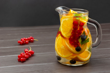 Redcurrant and orange infused water in glass jug. Sprig of red currant on table. copyspace. Dark wooden background.の写真素材