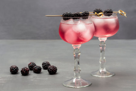 Two misted wine glasses with cooling drink and ice. Blackberry on skewer on wine glass. Blackberry table. flat lay. gray backgroundの写真素材