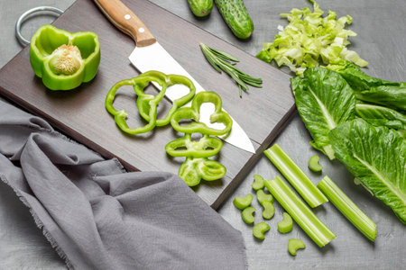 Chopped green pepper, kitchen knife and cutting board. Lettuce leaves and celery stalks on the table. flat lay. gray background.の写真素材