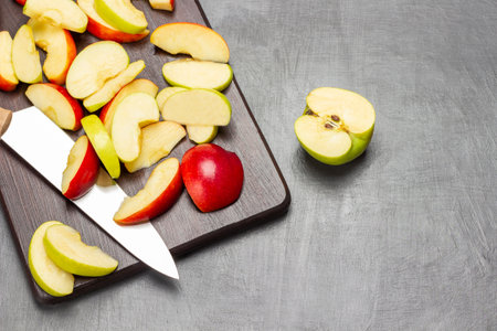 Half a green apple. Slices of green and red apples and kitchen knife on cutting board. copyspace. flat lay. gray backgroundの写真素材