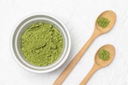Matcha green tea powder in a bowl and two wooden spoons. flat lay. white background