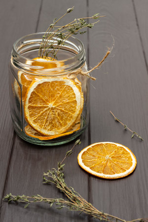 Orange chips in a glass jar. Dry sprigs of thyme on the table. Dark wooden background.の写真素材