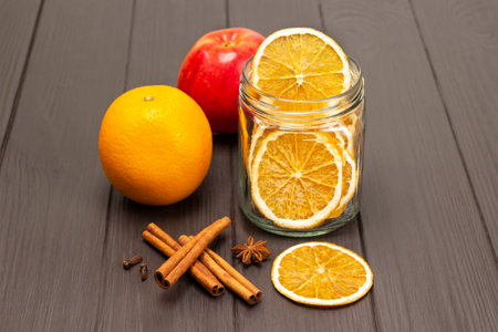 Orange chips in a glass jar. Raw orange and fresh apple. Cinnamon sticks and star anise on the table. copyspace. Dark wooden background.の写真素材