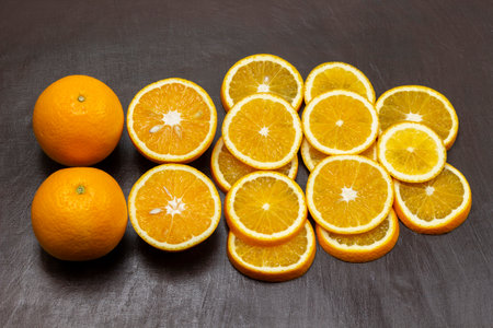 Two whole oranges, sliced orange on a brown background. flat layの写真素材