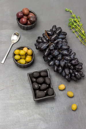 Olives in bowls. Bunch of black grapes, sprig of thyme and spoon on table. flat lay. gray backgroundの写真素材