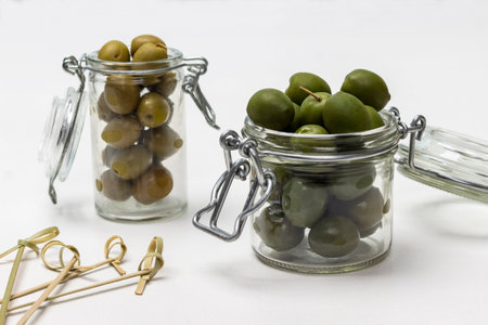 Olives in glass jars. Skewers on the table. white background.の写真素材