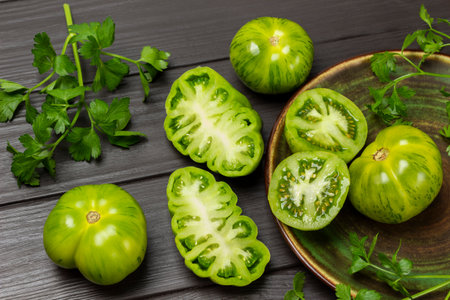 Parsley sprigs, green tomatoes in a plate and on the table. Dark wooden background.の写真素材
