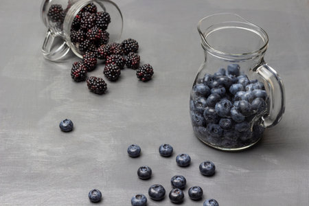 Blueberries in a decanter with water. Blackberries are scattered from a glass. Berries on the table. gray background.の写真素材