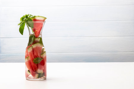 Slices of watermelon and a sprig of green basil in a decanter of water. copyspace. white background.の写真素材