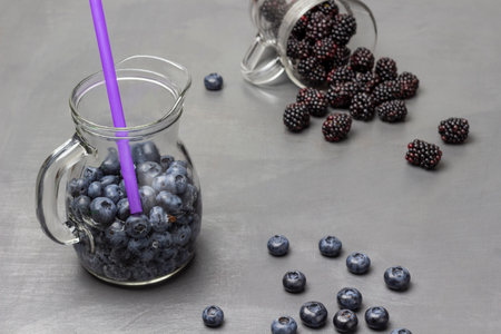 Berry summer drink made from berries and a straw in a decanter. Blackberries are scattered from a glass. gray background.の写真素材