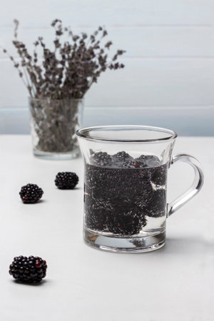 Blackberry summer drink in a glass mug. Lavender in glass. Blackberries on table. white background.の写真素材