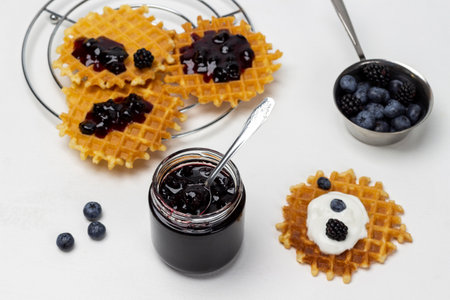 A jar of jam. Jam on waffles. Blackberries and blueberries in metal bowl on table. white background.の写真素材
