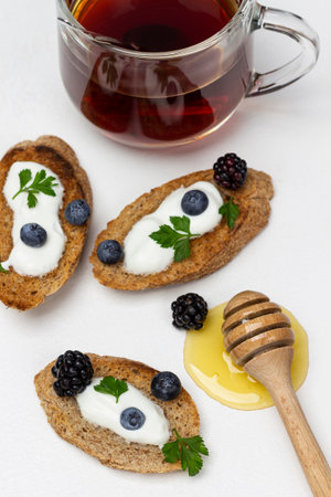 Croutons with cream and berries. Honey and honey stick. A cup of tea. white background.の写真素材