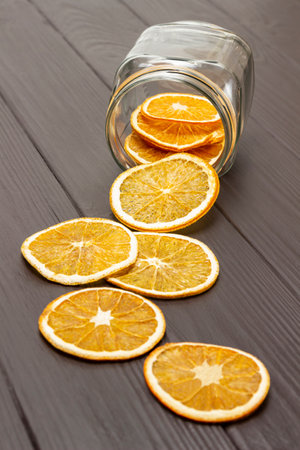Dry orange slices are scattered from a glass jar on the table. top view. Dark wooden background.の写真素材