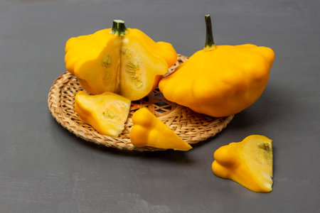Whole and cut yellow zucchini on a wicker plate. Zucchini slices on the table. gray background.の写真素材