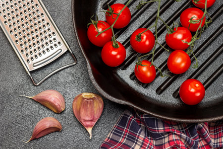 Cherry tomatoes in a pan. Garlic cloves, grater and napkin. flat lay. Black background.の写真素材