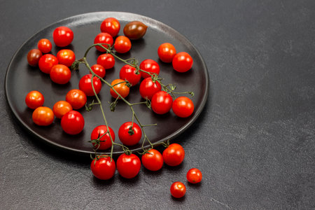 Twig of red cherry tomatoes on a black plate. copyspace. flat lay. Black background.の写真素材
