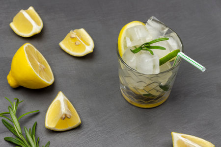 Glass of summer drink with ice and lemon. Slices of lemon on the table. flat lay. gray background.の写真素材
