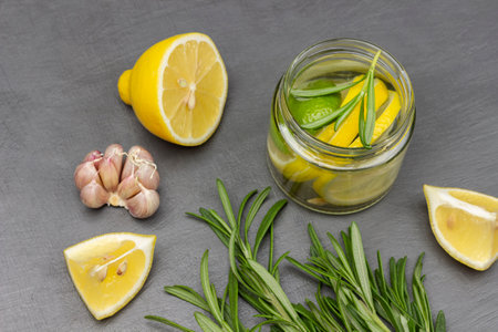 Garlic, rosemary sprigs and lemon on the table. Lemon drink in a glass jar. flat lay. gray background.の写真素材