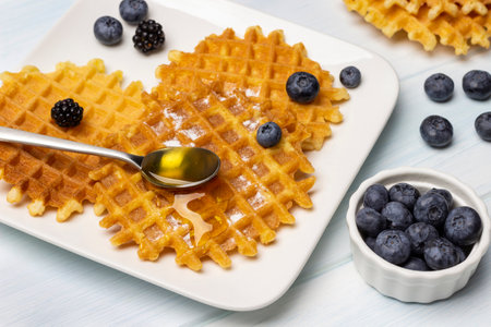 Blueberries in a white bowl. Spoon of honey, waffles and berries on a plate. white background.の写真素材