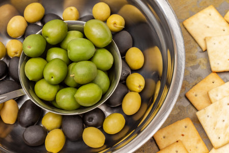Green and black olives in a metal bowl. Crackers on the table. flat lay.の写真素材