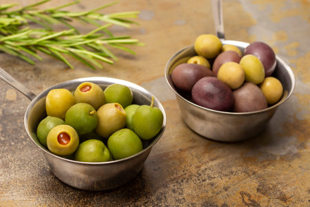 Dark and green olives in two metal bowls. Rosemary sprigs. Rusty backgroundの写真素材