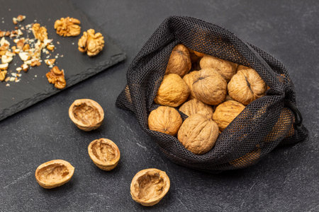 Walnuts in a reusable bag. Nut shells on the table, nut kernels on a black stone board. Black background.の写真素材