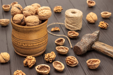Walnuts in a wooden bowl. Shell and hammer on the table. Dark wooden background.の写真素材