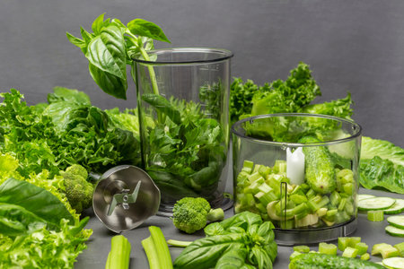 Blender and set of lettuce leaves, basil, celery stalks for making smoothies. gray background
