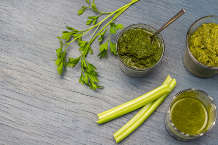Celery stalks, parsley sprigs, glasses with mixed vegetables. copy spse. flat lay. gray background.の写真素材