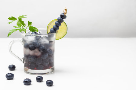 Misted glass with infused blueberry water and ice. Lime wedge on the edge of the glass and blueberries on skewer. copyspace. white background.の写真素材