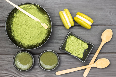 Measuring spoon in bowl with matcha powder. Matcha green tea and macaroni cakes and wooden spoons on table. flat lay. dark wooden backgroundの写真素材