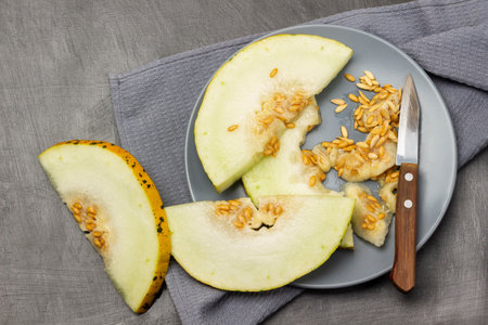 Melon slices with seeds and a knife on a gray plate. Gray napkin. flat lay. gray background.の写真素材