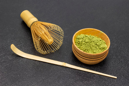Matcha green tea powder in wood bowl. Bamboo whisk and measuring spoon. top view. black backgroundの写真素材