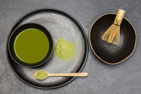 Bamboo whisk in a bowl. Wooden spoon with matcha powder and black bowl with green matcha tea. flat lay. black backgroundの写真素材