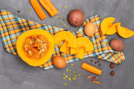 Half pumpkin and sliced pieces of pumpkin on napkin. Potatoes and carrots on table. flat lay. gray background.の写真素材