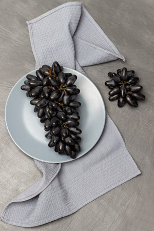 Gray plate with black grapes on a gray napkin. gray background.の写真素材